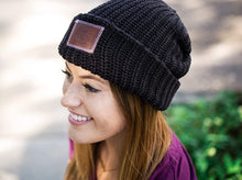 Load image into Gallery viewer, This black beanie features a red maple leather patch debossed with the Love Your Melon logo on the front. These beanies are very cozy and warm and have a slouchier fit. Details: Yarn Color: Black Sizing: 9” x 11” standard when uncuffed. One Size. Content: 99% Cotton 1% LYCRA® Care: Machine wash cold. Use mild detergent. Tumble dry on high.