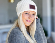 Load image into Gallery viewer, This white speckled beanie features a red maple leather patch debossed with the Love Your Melon logo on the front. These beanies are very cozy and warm and have a slouchier fit. Details: Yarn Color: Natural & White Sizing: 9” x 11” standard when uncuffed. One Size. Content: 99% Cotton 1% LYCRA® Care: Machine wash cold. Use mild detergent. Tumble dry on high.