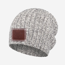 Load image into Gallery viewer, This black speckled beanie features a red maple leather patch debossed with the Love Your Melon logo on the front. These beanies are very cozy and warm and have a slouchier fit.  Details:  Yarn Color: Natural &amp; Black  Sizing: 9” x 11” standard when uncuffed. One Size.  Content: 99% Cotton 1% LYCRA®  Care: Machine wash cold. Use mild detergent. Tumble dry on high.
